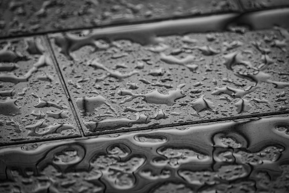 Grayscale close-up image of wet tiles with water droplets creating an abstract texture.
